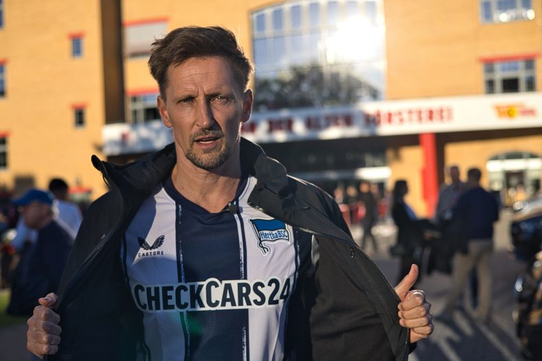 Thomas Melchior muestra una camiseta de Hertha Berlín al charla con un hincha del rival Union Berlín sobre apuestas deportivas, el domingo 28 de septiembre de 2025. (AP Foto/Ciaran Fahey)