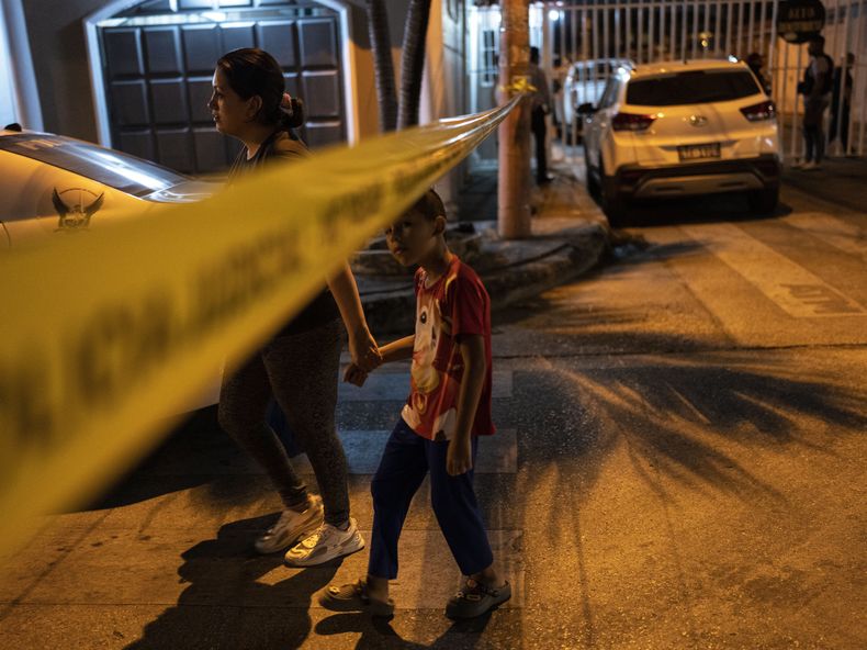 Residentes cruzan el precinto policial de la escena de un asesinato para llegar a su casa, en Durán, una ciudad ubicada frente a Guayaquil, Ecuador, el 28 de septiembre de 2023. Según la policía, un conductor fue baleado y trasladado a un hospital. (AP Foto/Rodrigo Abd)