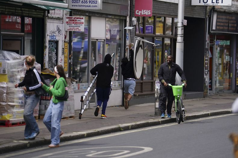 Se retiran corriendo con una nueva obra de arte de Banksy, que representa un lobo aullando pintado en una antena parabólica que se colocó en el techo de una tienda en Peckham, al sur de Londres, el jueves 8 de agosto de 2024. (Jordan Pettitt/PA via AP)