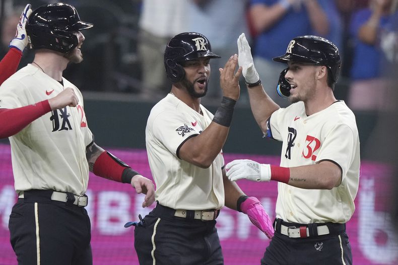 Evan Carter, derecha, de los Rangers de Texas, celebra con Jonah Heim, izquierda, y Leody Taveras, quien anotó en su cuadrangular en contra de los Marineros de Seattle durante la segunda entrada del juego de béisbol, en Arlington, Texas, el viernes 22 de septiembre de 2023. (AP Foto/LM Otero)
