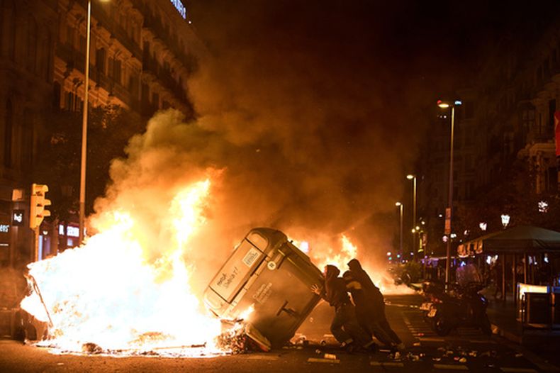 Manifestantes incendian contenedores de basura durante enfrentamientos con la policía tras una manifestación por la crisis de vivienda en España, en Barcelona, España, el lunes 5 de octubre de 2026, horas después de que el presidente de gobierno Pedro Sánchez anunciara elecciones generales anticipadas. (AP Foto/Emilio Morenatti)