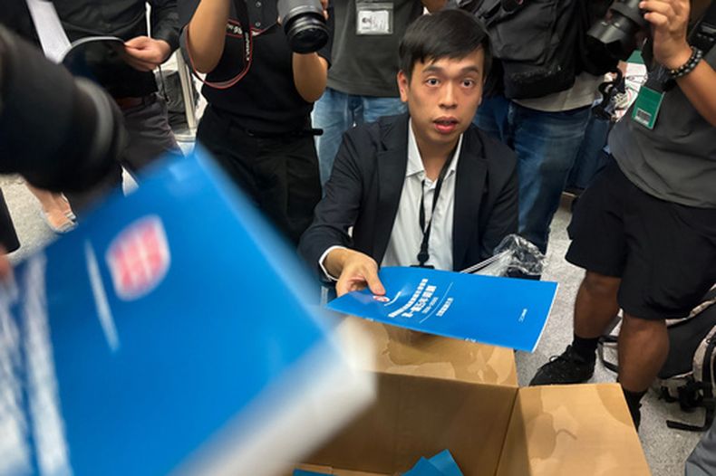 Un hombre reparte a periodistas documentos de consulta pública para el primer plan quinquenal de Hong Kong, en la sede del gobierno en Hong Kong, el lunes 15 de junio de 2026. (AP Foto/Kanis Leung)