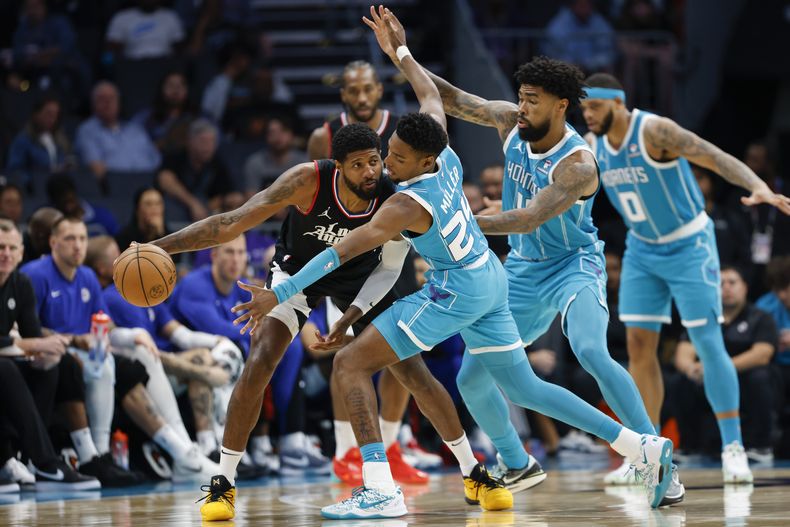 Paul George, izquierda, de los Clippers de Los Ángeles, busca a quien pasarle el balón ante la presión defensiva de Brandon Miller (24) y Nick Richards, de los Hornets de Charlotte, durante la segunda mitad del juego de baloncesto de la NBA, el domingo 31 de marzo de 2024, en Charlotte, Carolina del Norte. (AP Foto/Nell Redmond)