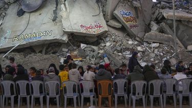 Palestinos sentados en una mesa grande rodeada por los escombros de viviendas y edificios destruidos, reunidos para el iftar, la comida que rompe el ayuno, en el primer día del Ramadán en Rafah, en el sur de la Franja de Gaza, el sábado 1 de marzo de 2025 (AP Foto/Abdel Kareem Hana)