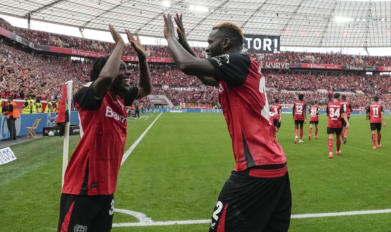 Victor Boniface (derecha) celebra con Jeremie Frimpong tras anotar el cuarto gol del Bayer Leverkusen en la victoria 4/3 ante Wolfsburgo en la Bundeslig, el domingo 22 de septiembre de 2024. (AP Foto/Martin Meissner)