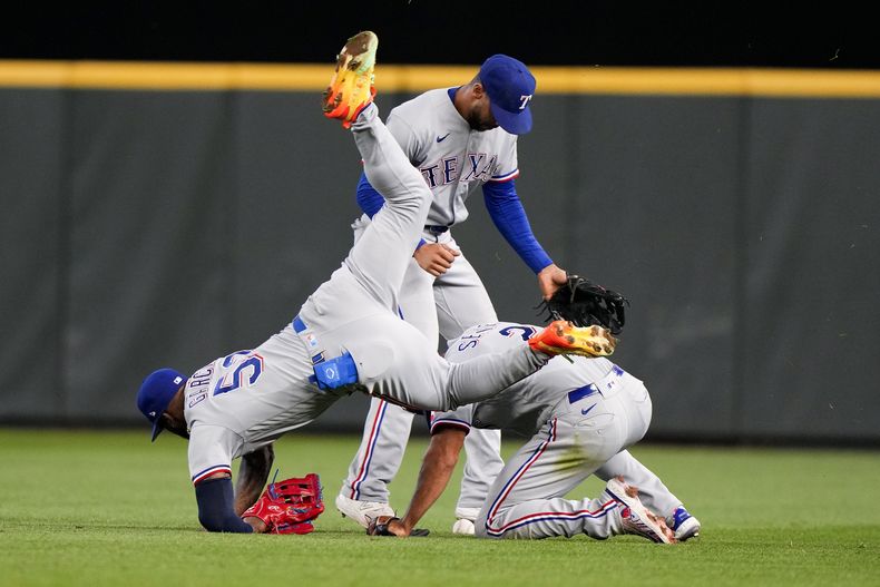 El cubano Adolis García, de los Rangers de Texas, tropieza con su compañero Marcus Semien, junto al dominicano Leody Taveras, tras la victoria sobre los Marineros de Seattle, el sábado 30 de septiembre de 2023 (AP Foto/Lindsey Wasson)