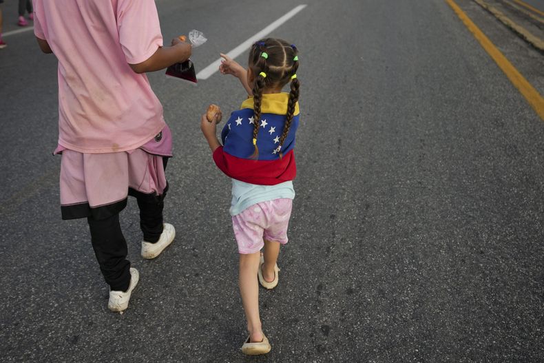 Una niña envuelta en una bandera venezolana camina por la carretera Huixtla con una caravana de migrantes que esperan llegar a la frontera norte de México y finalmente a Estados Unidos, en Huehuetán, sur de México, el miércoles 6 de noviembre de 2024. (Foto AP/Moisés Castillo)