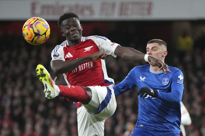 Bukayo Saka, izquierda, del Arsenal, patea el balón frente a Vitaliy Mykolenko, de Everton, durante el partido de la Liga Premier de Inglaterra entre Arsenal y Everton en el estadio Emirates, en Londres, el sábado 14 de diciembre de 2024. (AP Foto/Kin Cheung)