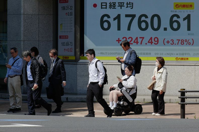 Varias personas caminan en Tokio frente a una pantalla electrónica que muestra el índice Nikkei de Japón en una correduría de valores el jueves 7 de mayo de 2026. (AP Foto/Eugene Hoshiko)