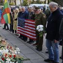 Personas con la bandera nacional estadounidense acuden a presentar sus condolencias a los tres soldados hallados muertos el lunes en un campo de entrenamiento de Pabrade, cerca de la embajada de Estados Unidos en Vilna, Lituania, martes 1 de abril de 2025. (AP foto/Mindaugas Kulbis)
