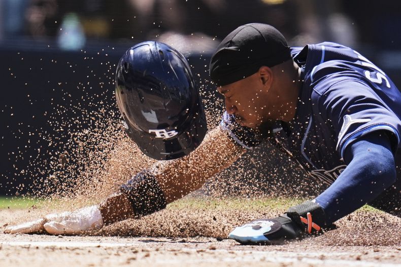 Chandler Simpson, de los Rays de Tampa Bay, se desliza para anotar desde la tercera base tras un lanzamiento descontrolado durante la quinta entrada de un juego de béisbol contra los Padres de San Diego, el domingo 27 de abril de 2025, en San Diego. (AP Foto/Gregory Bull)