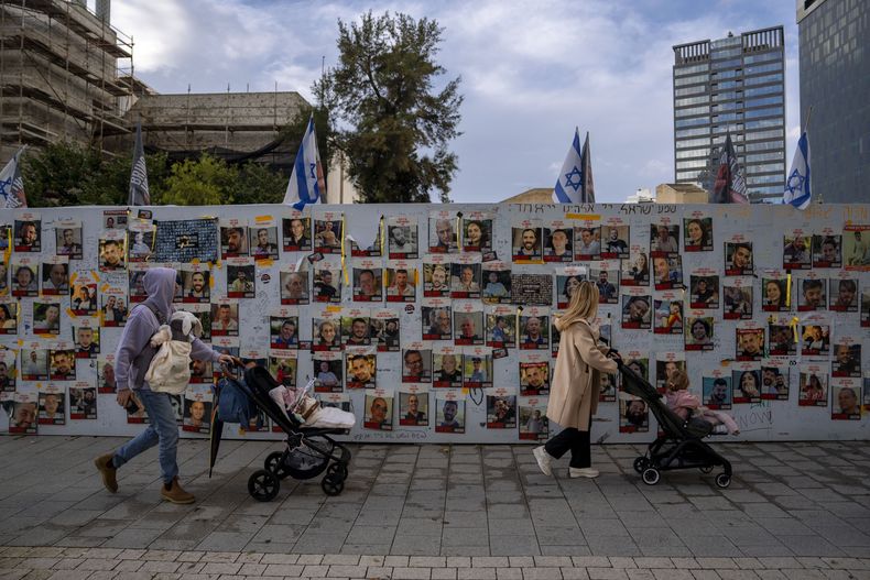 Varias personas caminan frente a un muro con fotografías de rehenes, principalmente civiles israelíes, secuestrados por Hamás en sus ataques contra Israel, ocurridos el 7 de octubre de 2022, en Tel Aviv, Israel, el mipercoles 31 de enero de 2024. (AP Foto/Oded Balilty)
