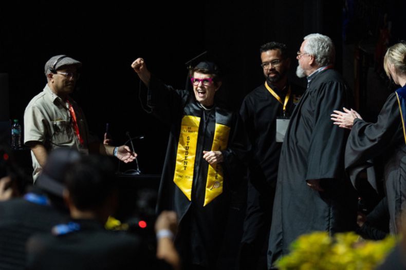 La leyenda del tenis Billie Jean King, centro, alza el puño luego de escuchar su nombre para recibir su título durante la ceremonia de graduación de California State University, Los Ángeles, el lunes 18 de mayo de 2026, en Los Ángeles. (AP Foto/Jae C. Hong)