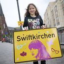 La estudiante Aleshanee Westhoff muestra un cartel de la ciudad Swiftkirchen en honor a Taylor Swift en Gelsenkirchen, Alemania, el martes 2 de julio de 2024. Los swifties están a punto de apoderarse de la ciudad alemana de Gelsenkirchen, donde la superestrella estadounidense Taylor Swift dará tres conciertos de su Eras Tour a finales de este mes. En honor al cantante, la ciudad se rebautizó como Swiftkirchen temporalmente para dar la bienvenida a las decenas de miles de fans. (Bernd Thissen/dpa via AP)