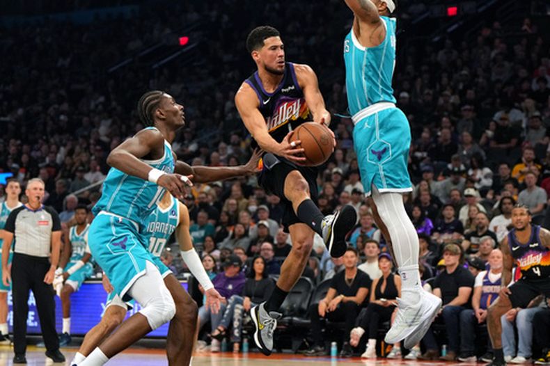 Devin Booker, base de los Suns de Phoenix, conduce el balón entre Moussa Diabaté, Josh Green (10) y Miles Bridges, de los Hornets de Charlotte, durante la primera mitad de un juego de baloncesto de la NBA, el domingo 8 de marzo de 2026, en Phoenix. (Foto AP/Rick Scuteri)