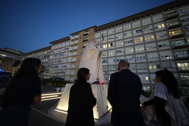 Varias personas se reúnen para rezar por el papa León XIV junto a una estatua del San Juan Pablo II, en el hospital Agostino Gemelli, donde está hospitalizado, en Roma, el 16 de octubre de 2026. (AP Foto/Andrew Medichini)