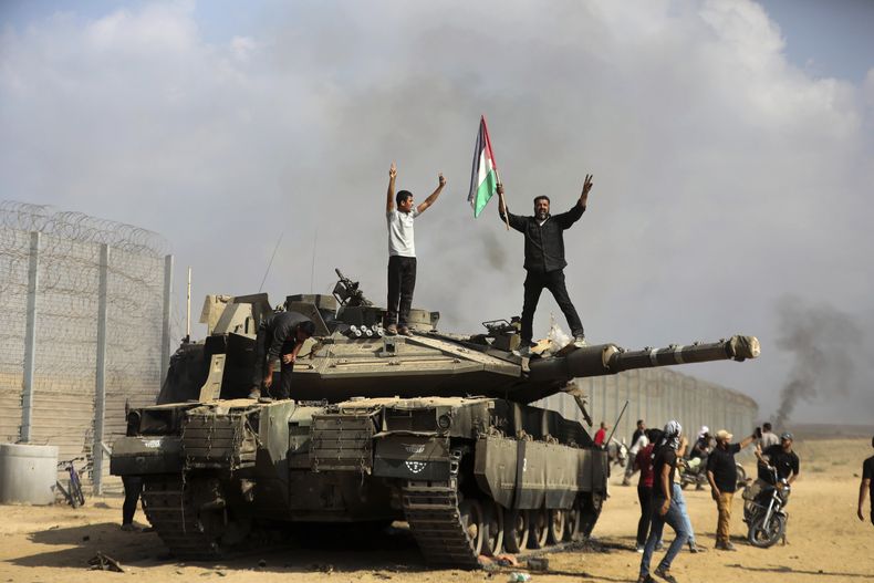 Palestinos ondean una bandera nacional y celebran junto a un taque israelí destruido en la valla fronteriza que separa la Franja de Gaza de Israel, al este de Khan Younis, el 7 de octubre de 2023. (AP Foto/Yousef Masoud)