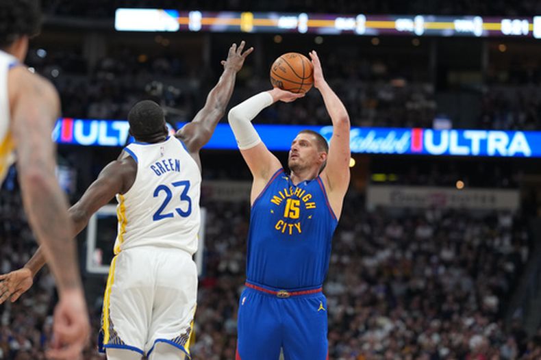 Nikola Jokić, derecha, de los Nuggets de Denver, se alza para disparar mientras Draymond Green, de los Warriors de Golden State, defiende durante la primera mitad del juego de baloncesto de la NBA, el domingo 29 de marzo de 2026, en Denver. (AP Foto/David Zalubowski)