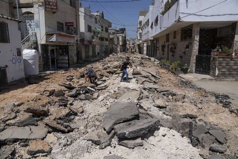 Dos escolares palestinos cruzan una calle dañada durante el operativo del ejército israelí en julio en el campo de refugiados de Jenin, Cisjordania, 3 de agosto de 2023. (AP Foto/Nasser Nasser)