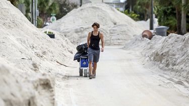 David DeMeza camina con sus pertenencias entre calles cubiertas de arena arrastrada por el huracán Helene, el 2 de octubre de 2024, en Treasure Island, Florida (AP Foto/Mike Carlson)