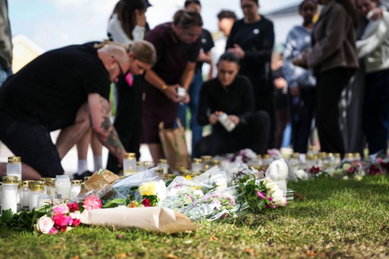 Varias personas depositan flores y velas en un sitio improvisado de homenaje a las afueras de una escuela en Fagersta, Suecia, el sábado 22 de agosto de 2026, un día después que un adolescente de 18 años, armado con una espada, atacara el centro educativo, causando la muerte de una persona e hiriendo gravemente a otras dos. (Magnus Lejhall/TT vía AP)