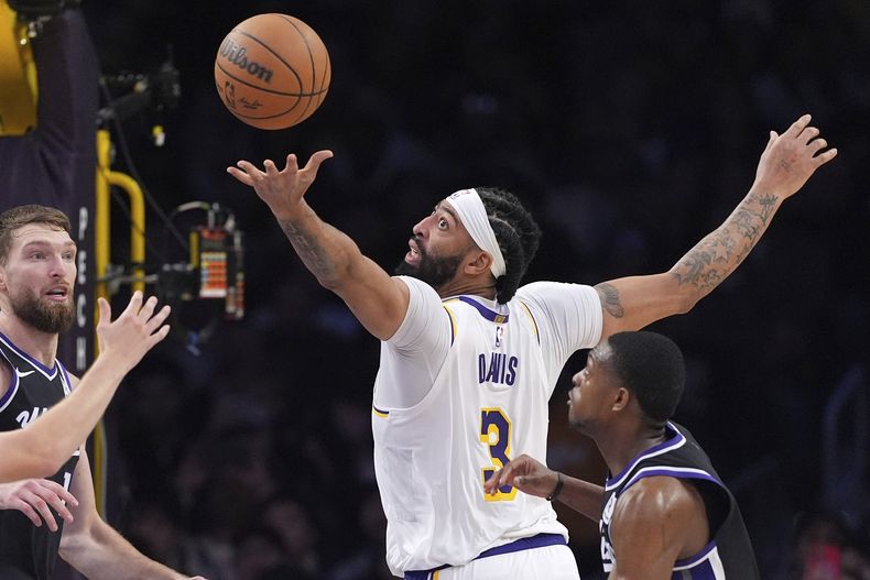 Anthony Davis, alero de los Lakers de Los Ángeles, busca hacerse de un balón perdido entre Domantas Sabonis y DeAaron Fox, de los Kings de Sacramento, el sábado 28 de diciembre de 2024 (AP Foto/Mark J. Terrill)