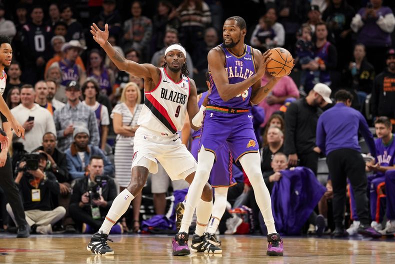 El alero de los Trail Blazers de Portland, Jerami Grant (9), defiende al alero de los Suns de Phoenix, Kevin Durant (35), durante la primera mitad de un partido de baloncesto de la NBA, el domingo 15 de diciembre de 2024, en Phoenix. (AP Foto/Samantha Chow)