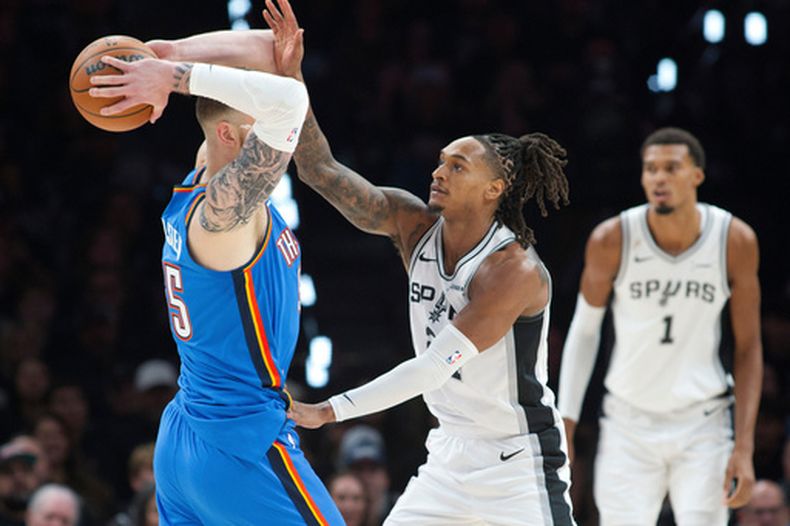 El pívot del Thunder de Oklahoma City, Isaiah Hartenstein, a la izquierda, busca dar un pase mientras es defendido por el guardia de los Spurs de San Antonio, Devin Vassell, durante la primera mitad de un partido de básquetbol de la NBA, el martes 20 de octubre de 2026, en San Antonio. (Foto AP/Darren Abate)
