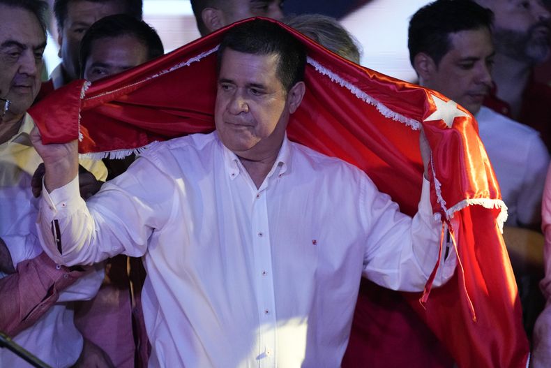 El expresidente Horacio Cartes cubierto con una bandera del gobernante Partido Colorado tras el cierre de votaciones en las elecciones generales, en Asunción, Paraguay, el domingo 30 de abril de 2023. (AP Foto/Jorge Sáenz)