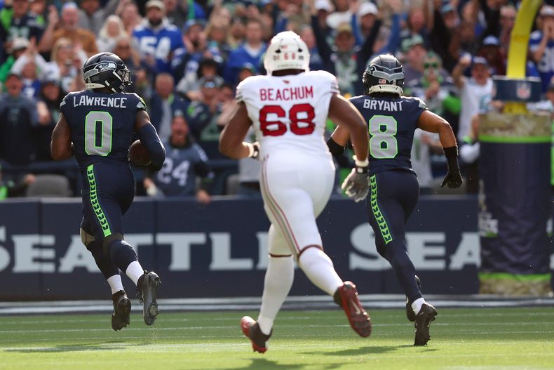 Demarcus Lawrence (0), de los Seahawks de Seattle, devuelve un balón suelto hasta la zona de anotación acompañado de Coby Bryant (8) y ante la mirada de Kelvin Beachum (68), de los Cardinals de Arizona, durante la primera mitad del partido de la NFL, el domingo 9 de noviembre de 2025, en Seattle. (AP Foto/Maddy Grassy)