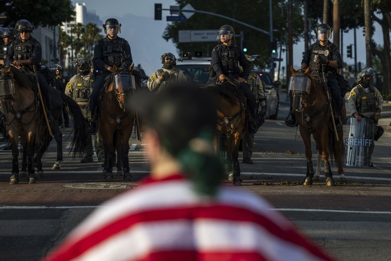 Agentes de policía, frente a manifestantes en el exterior del edificio del ayuntamiento durante protestas contra las redadas migratorias federales, el 11 de junio de 2025, en Los Ángeles. (AP Foto/Ethan Swope)