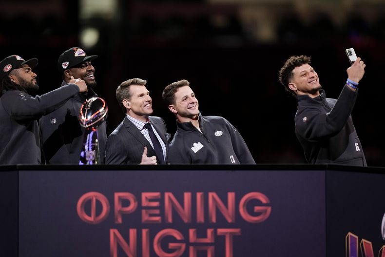 Patrick Mahomes (15), quarterback de los Chiefs de Kansas City, toma una foto con Brock Purdy (13), quarterback de los 49ers de San Francisco, Scott Hanson, de NFL Network, Chris Jones y Fred Warner, durante la noche de apertura del Super Bowl 58, el lunes 5 de febrero de 2024, en Las Vegas. (AP Foto/Charlie Riedel)