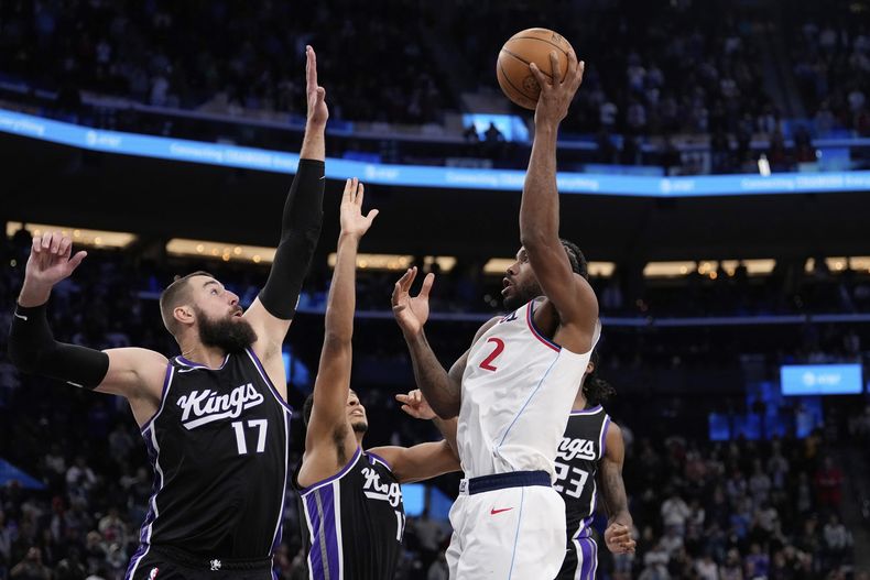 Kawhi Leonard, derecha, de los Clippers de Los Ángeles, tira y encesta el tiro ganador sperando la bocina frente a Jonas Valanciunas, izquierda, y Keegan Murray, de los Kings de Sacramento, segundo a la izquierda, en el tiempo extra durante el partido de baloncesto de la NBA, el domingo 9 de marzo de 2025, en Inglewood, California. (AP Foto/Mark J. Terrill)
