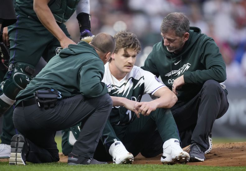 Los asistentes médicos atienden al lanzador abridor de los Rockies de Colorado, Ryan Feltner, después de haber sido golpeado por un batazo de Nick Castellanos, de los Filis de Filadelfia, quien bateó sencillo durante la segunda entrada del juego de béisbol el sábado 13 de mayo de 2023, en Denver. (AP Foto/David Zalubowski)