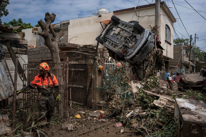 Un rescatista, miembro de la brigada de voluntarios Topos, trabaja cerca de un automóvil colgado de una cerca junto a una casa dañada en Poza Rica, México, el lunes 13 de octubre de 2025, tras lluvias torrenciales. (AP Foto/Félix Márquez)