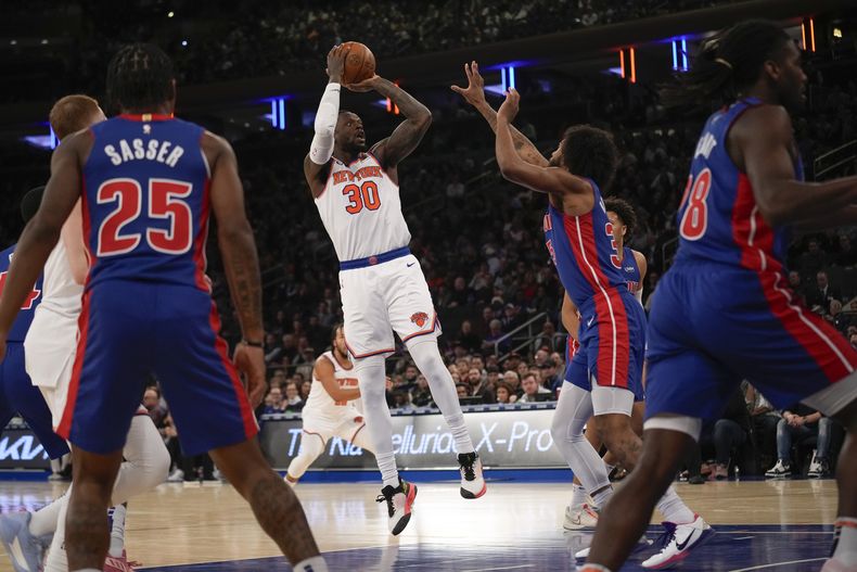 Julius Randle de los Knicks de Nueva York salta hacia atrás para lanzar el balón mientras lo defienden los jugadores de los Pistons de Detroit el jueves 30 de noviembre del 2023. (AP Foto/Seth Wenig)