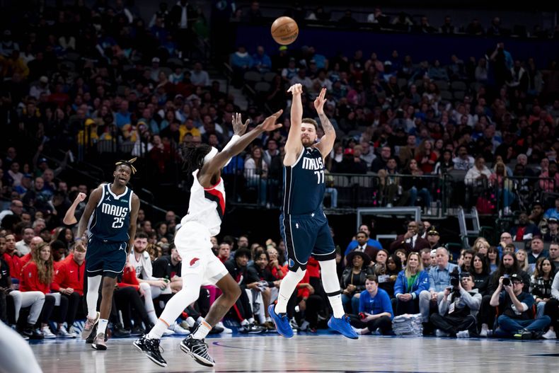 ARCHIVO - Foto del 16 de diciembre del 2022, el base de los Mavericks de Dallas Luka Doncic lanza un balón desde larga distancia en la bocina frente al alero de los Trail Blazers de Portland Jerami Grant. (AP Foto/Emil Lippe, Archivo)