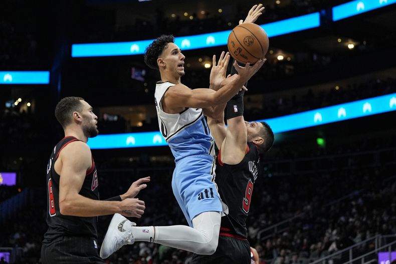 El alero de los Hawks de Atlanta Zaccharie Risacher salta con el balón frente al pívot Nikola Vucevic de los Bulls de Chicago en el encuentro del jueves 26 de diciembre del 2024. (AP Foto/Mike Stewart)