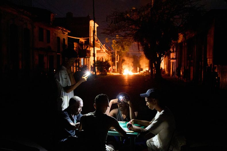 Varias personas se iluminan con sus teléfonos mientras juegan al dominó, al tiempo que arde en una calle de La Habana, Cuba, una hoguera provocada por residentes que protestaban contra los prolongados cortes de luz. (Foto AP/Ramón Espinosa)