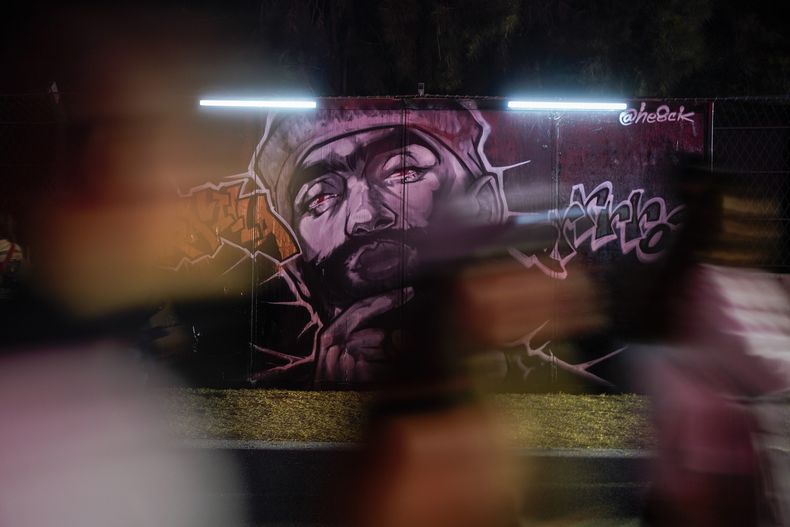 Fans caminan frente a un grafiti en el Coca-Cola Flow Fest en la Ciudad de México el sábado 23 de noviembre de 2024. (Foto AP/Félix Márquez)