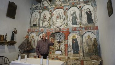 El maestro santero Félix López, un artista entrenado en la tradición de escultura y pintura religiosa de Nuevo México, que se remonta siglos atrás, habla durante una entrevista el domingo 16 de abril de 2023 frente a un retablo de la década de 1810 que él limpió y preservó, en la misión del Santo Rosario en Truchas, Nuevo México. (AP Foto/Giovanna DellOrto)