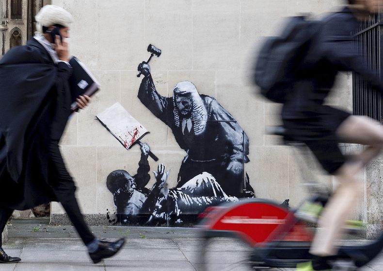 Fotografía sin fecha publicada por Banksy de la nueva obra de arte del artista que retrata a un juez golpeando a un manifestante con un mazo en los Tribunales Reales de Justicia de Londres. (Banksy via AP)
