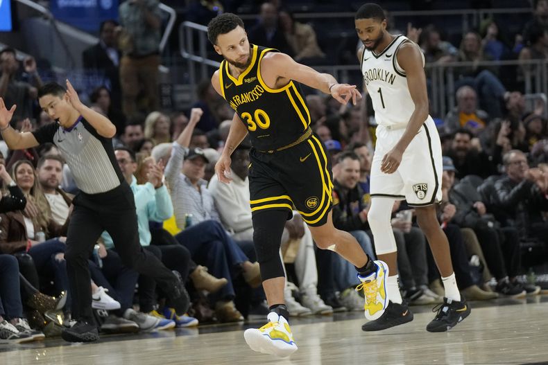 Stephen Curry, base de los Warriors de Golden State, festeja luego de atinar un triple, junto a Mikal Bridges, alero de los Nets de Brooklyn, el sábado 16 de diciembre de 2023 (AP Foto/Jeff Chiu)
