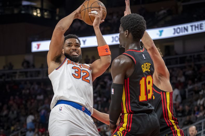 El pívot de los Knicks de Nueva York, Karl-Anthony Towns (32), maneja el balón contra el alero de los Hawks de Atlanta, Mouhamed Gueye (18), durante la primera mitad de un partido de baloncesto de la NBA, el sábado 5 de abril de 2025, en Atlanta. (AP Foto/Erik Rank)