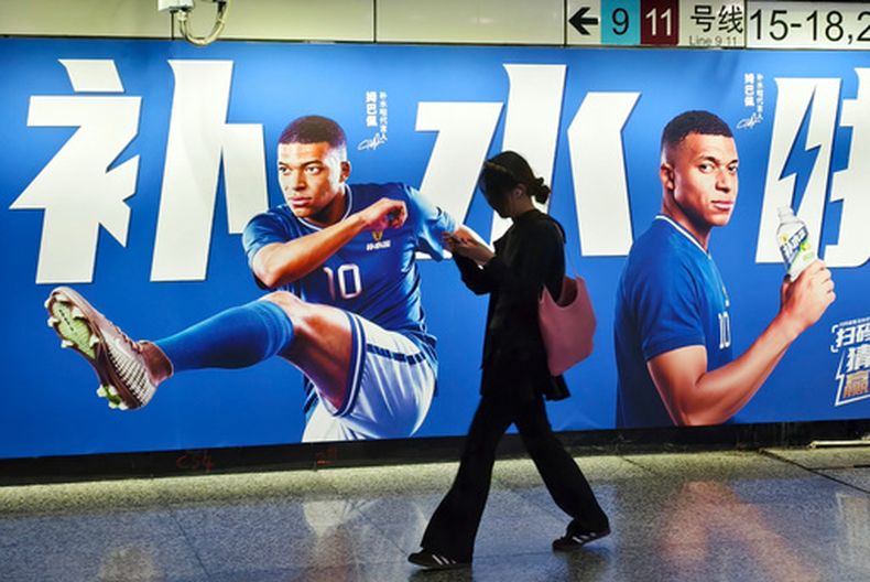 Una mujer camina frente a un cartel con publicidad de Kylian Mbappé en Shangái, el 30 de junio de 2026. (Chinatopix vía AP) CHINA OUT