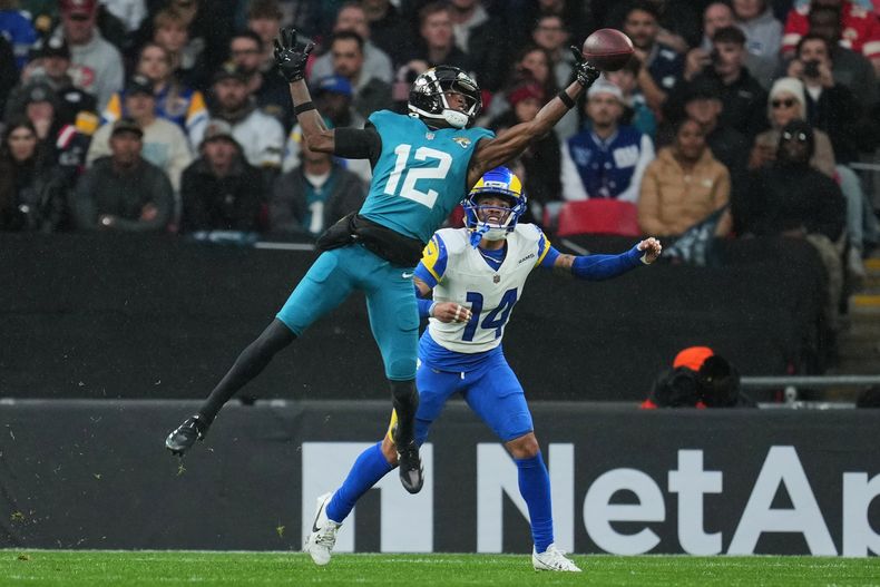 Travis Hunter (12), wide receiver de los Jaguars de Jacksonville, se estira para atrapar el balón mientras Cobie Durant (14), cornerback de los Rams de Los Ángeles, lo desafía durante la primera mitad de un juego de fútbol americano de la NFL en Londres, el domingo 19 de octubre de 2025. (AP Photo/Kin Cheung)
