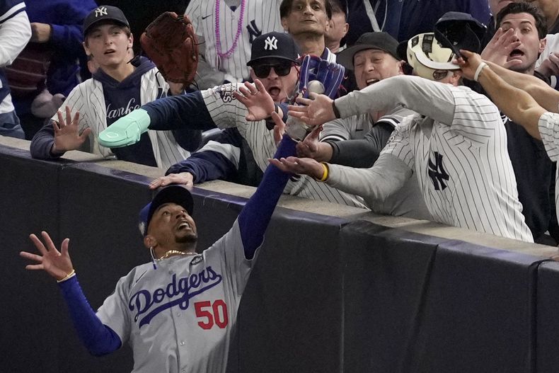 Fanáticos interfieren en un elevado de foul atrapado por el jardinero derecho Mookie Betts de los Dodgers de Los Ángeles ante los Yankees de Nueva York durante el primer inning del cuarto juego de la Serie Mundial, el martes 29 de octubre de 2024, en Nueva York. (AP Foto/Ashley Landis)
