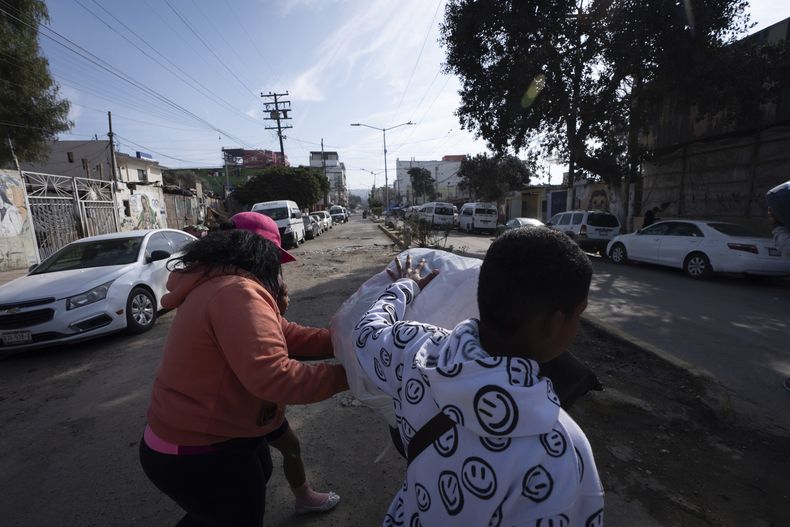 Margelis Rodríguez, a la izquierda, de Venezuela, empuja un carrito con la colada mientras su hijo Mickel endereza la carga camino de una lavandería cercana en Tijuana, México, el vienes 31 de enero de 2025. (AP Foto/Gregory Bull)