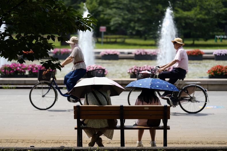 ARCHIVO – Personas con parasoles sentadas en una banca bajo el intenso sol en un parque de Tokio, el 8 de julio de 2024. (AP Foto/Eugene Hoshiko, Archivo)