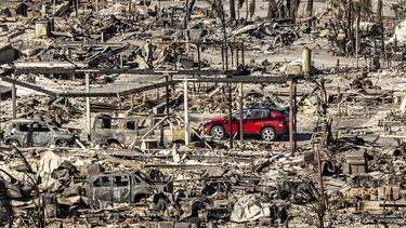 Un automóvil pasa junto a casas y vehículos destruidos por el incendio de Pacific Palisades Bowl Mobile Estates, el domingo 12 de enero de 2025, en Los Ángeles. (AP Foto/Noah Berger)